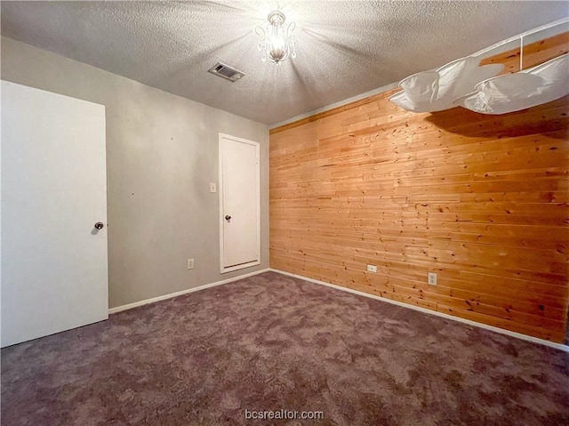 empty room featuring dark colored carpet, a textured ceiling, and wooden walls