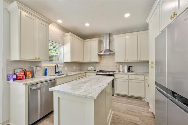 kitchen with wall chimney exhaust hood, stainless steel appliances, sink, light hardwood / wood-style floors, and a kitchen island