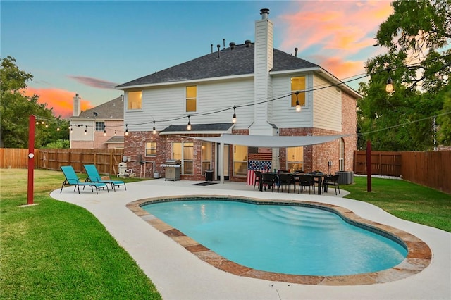 back house at dusk with a lawn, a fenced in pool, and a patio