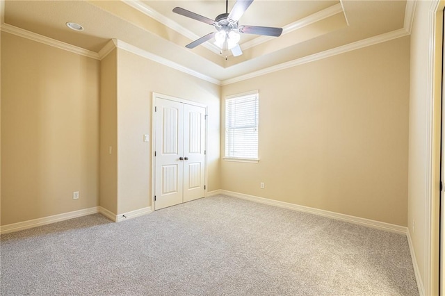 unfurnished bedroom with carpet flooring, ceiling fan, a tray ceiling, crown molding, and a closet