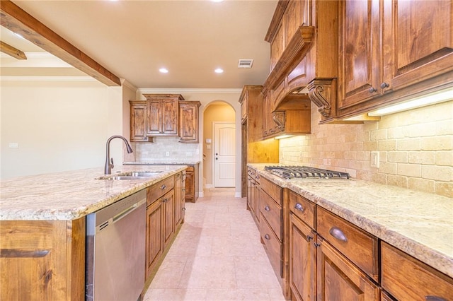 kitchen with sink, crown molding, appliances with stainless steel finishes, light stone counters, and an island with sink