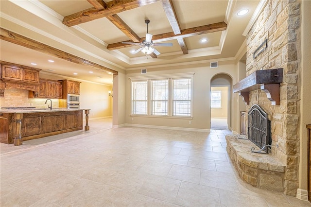 unfurnished living room with coffered ceiling, beam ceiling, ornamental molding, ceiling fan, and a fireplace