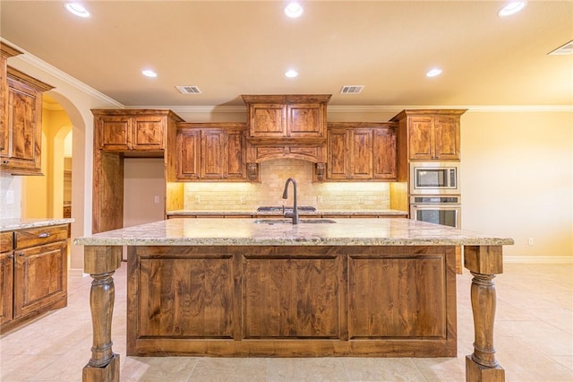 kitchen with light stone counters, stainless steel appliances, sink, and a center island with sink