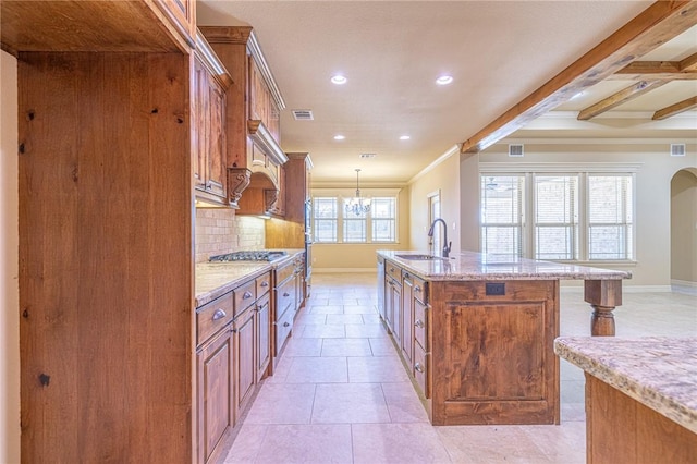 kitchen with sink, light stone counters, hanging light fixtures, a center island with sink, and decorative backsplash