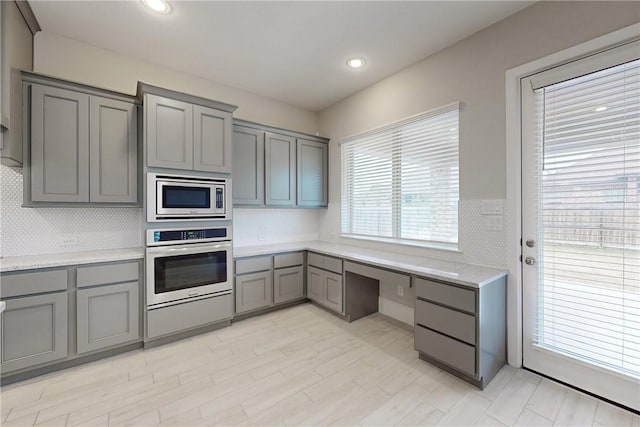 kitchen with gray cabinets, tasteful backsplash, built in desk, and appliances with stainless steel finishes