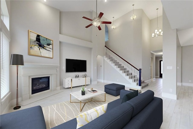 living room with ceiling fan with notable chandelier, a high ceiling, and light hardwood / wood-style flooring