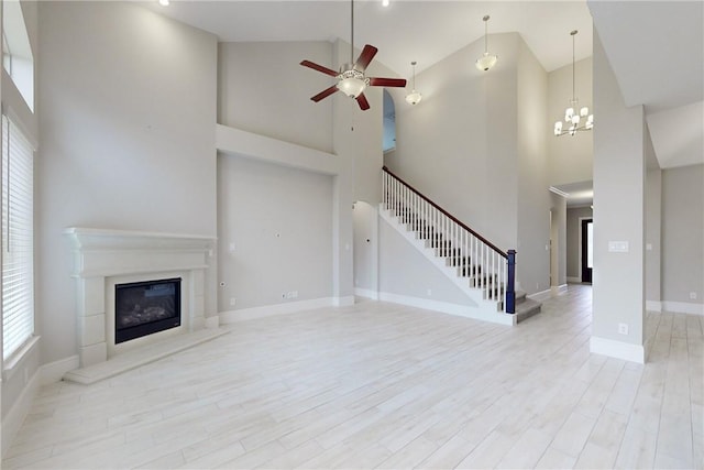 unfurnished living room featuring ceiling fan with notable chandelier, high vaulted ceiling, and light hardwood / wood-style floors