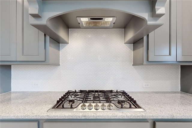 kitchen with wall chimney exhaust hood, decorative backsplash, gray cabinets, stainless steel gas cooktop, and light stone counters