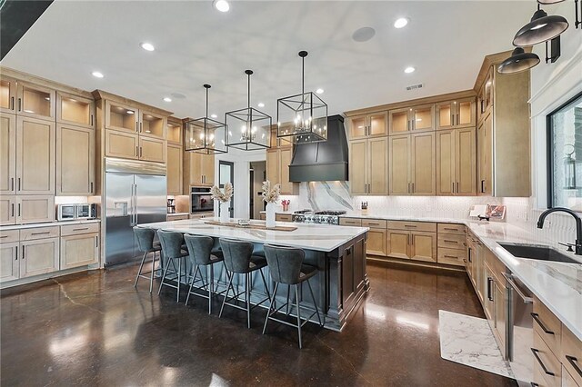 kitchen featuring appliances with stainless steel finishes, custom range hood, sink, a breakfast bar area, and an island with sink