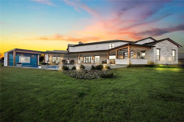 back house at dusk with a patio area and a lawn