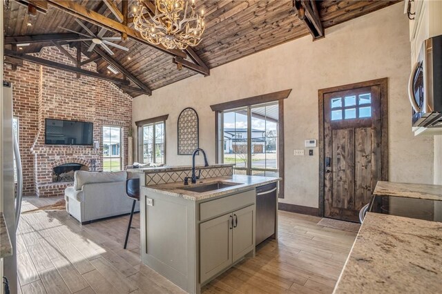 kitchen featuring appliances with stainless steel finishes, light wood-type flooring, a kitchen island with sink, and high vaulted ceiling