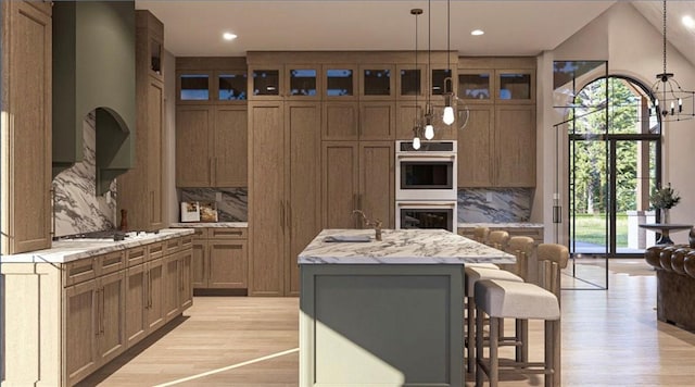 kitchen with tasteful backsplash, a kitchen bar, a kitchen island with sink, light stone counters, and stainless steel double oven