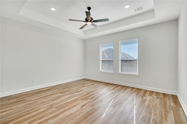 unfurnished room featuring light hardwood / wood-style flooring, a raised ceiling, and ceiling fan