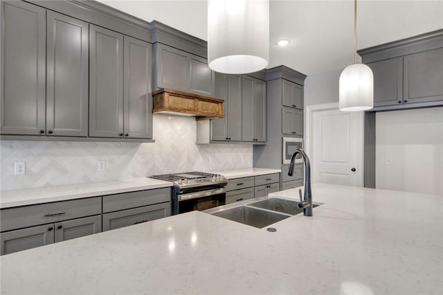 kitchen with gas stove, gray cabinetry, sink, light stone counters, and pendant lighting