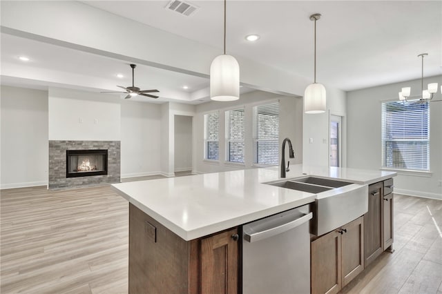 kitchen featuring a kitchen island with sink, dishwasher, hanging light fixtures, and light hardwood / wood-style flooring