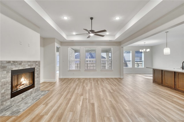 unfurnished living room featuring ceiling fan with notable chandelier, a tray ceiling, and light hardwood / wood-style flooring