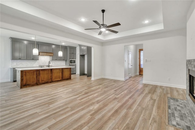 interior space featuring a tile fireplace, a raised ceiling, sink, ceiling fan, and light hardwood / wood-style floors