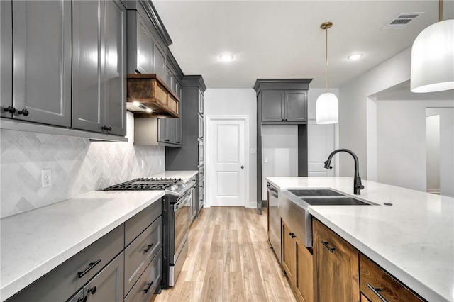 kitchen featuring light stone countertops, appliances with stainless steel finishes, sink, decorative light fixtures, and light hardwood / wood-style floors