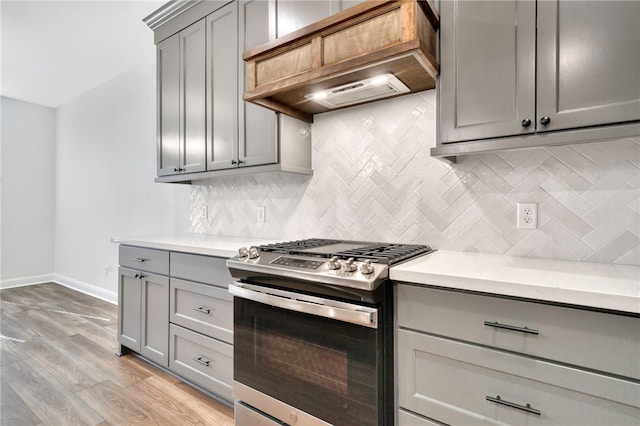 kitchen with decorative backsplash, stainless steel gas range oven, light wood-type flooring, and premium range hood