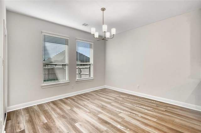 empty room with light hardwood / wood-style floors and a notable chandelier