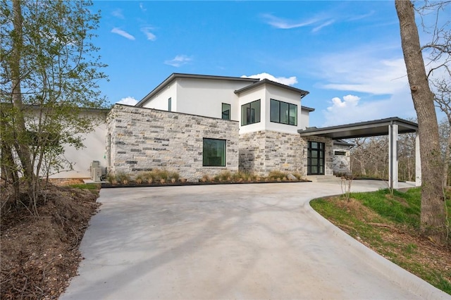 contemporary house featuring an attached carport, stone siding, driveway, and stucco siding