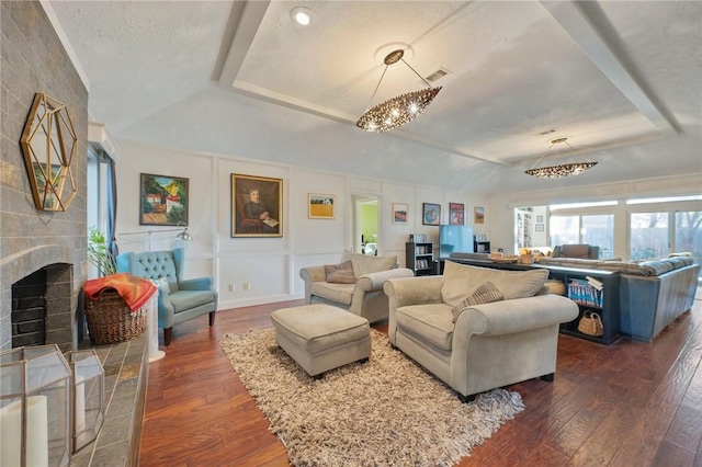 living room featuring a textured ceiling, dark hardwood / wood-style flooring, a fireplace, a chandelier, and a tray ceiling