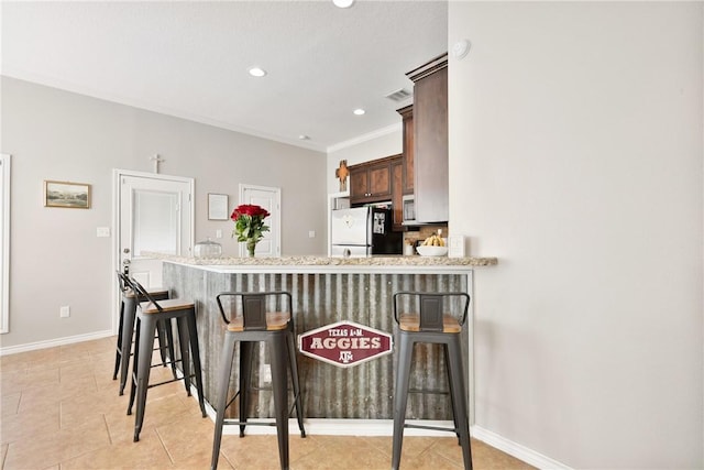 kitchen with light tile patterned floors, a breakfast bar area, refrigerator, and kitchen peninsula