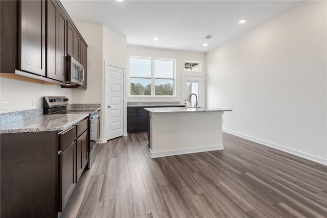 kitchen featuring dark hardwood / wood-style floors, sink, a kitchen island with sink, light stone counters, and stainless steel appliances