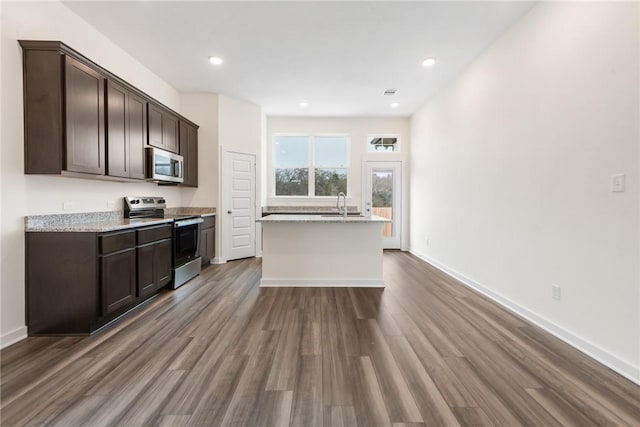 kitchen with stainless steel appliances, a kitchen island, hardwood / wood-style floors, and dark brown cabinetry