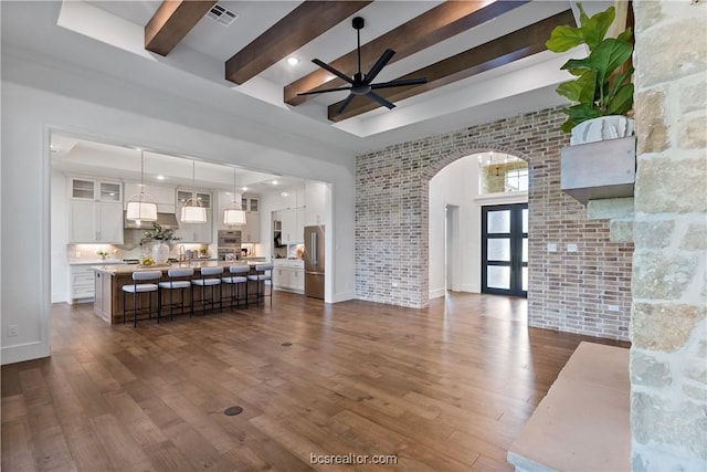 living room with beam ceiling, ceiling fan, french doors, dark hardwood / wood-style flooring, and brick wall