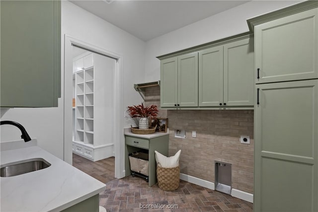 kitchen with backsplash, light stone countertops, sink, and green cabinetry