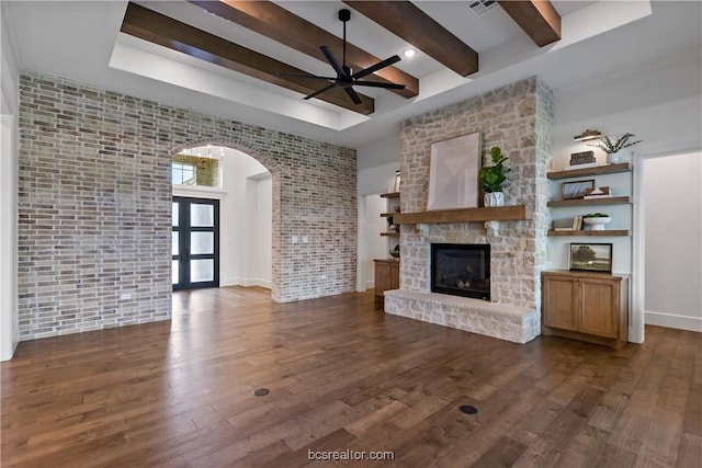 unfurnished living room with ceiling fan, beam ceiling, dark hardwood / wood-style flooring, and a fireplace