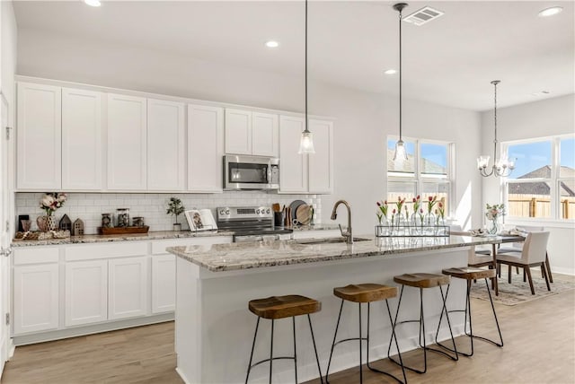 kitchen featuring white cabinets, light hardwood / wood-style flooring, an island with sink, and stainless steel appliances