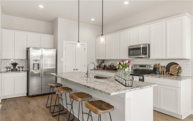 kitchen with decorative backsplash, stainless steel appliances, sink, a center island with sink, and white cabinetry