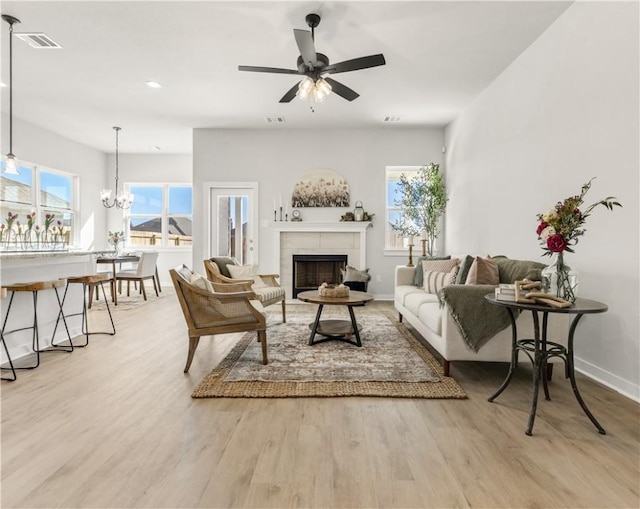 living room with a tile fireplace, light hardwood / wood-style flooring, and ceiling fan with notable chandelier