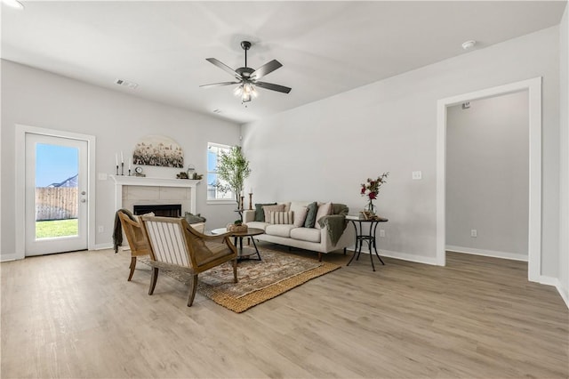 living room featuring ceiling fan, light hardwood / wood-style floors, a wealth of natural light, and a tiled fireplace