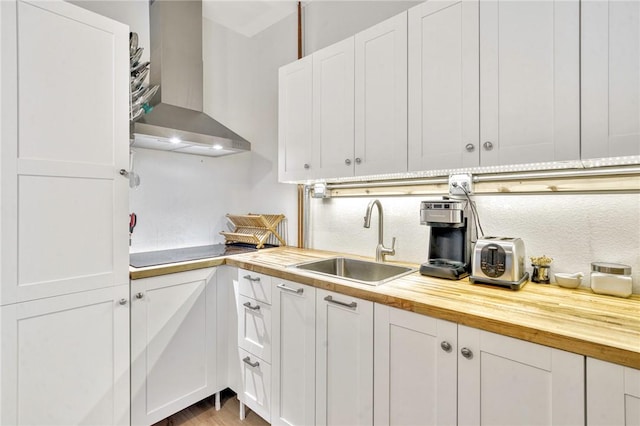 kitchen with butcher block countertops, white cabinetry, wall chimney exhaust hood, and sink