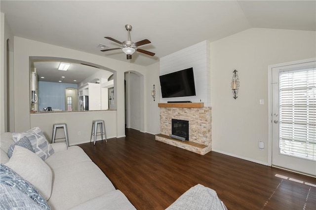 living room featuring lofted ceiling, a fireplace, wood finished floors, arched walkways, and a ceiling fan