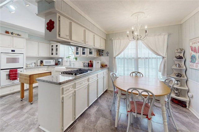 kitchen with light stone counters, a peninsula, white appliances, glass insert cabinets, and an inviting chandelier