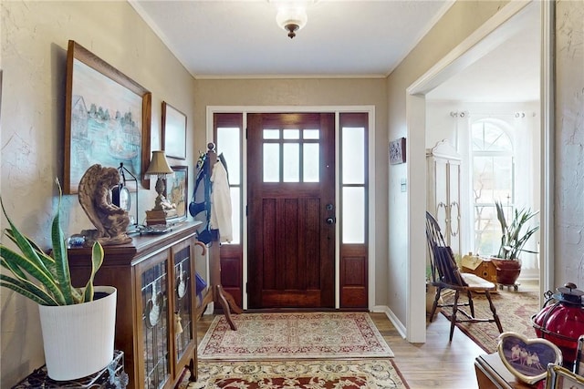 entrance foyer with ornamental molding, light wood-type flooring, and baseboards