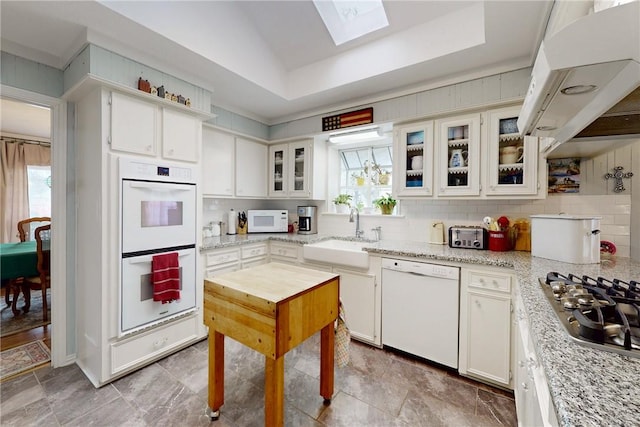 kitchen featuring white appliances, decorative backsplash, a raised ceiling, under cabinet range hood, and a sink