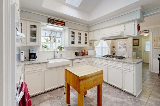 kitchen with under cabinet range hood, stainless steel gas cooktop, a peninsula, a sink, and dishwasher