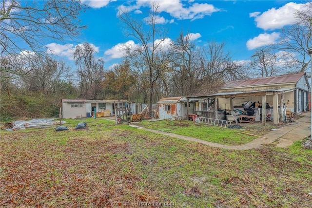 rear view of property featuring a lawn, a carport, and a shed