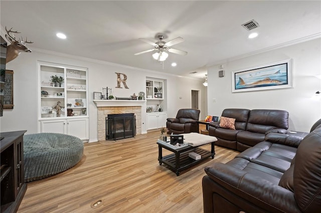 living room featuring ornamental molding, a ceiling fan, light wood-type flooring, a stone fireplace, and built in features