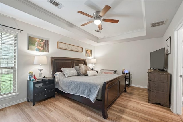 bedroom featuring a raised ceiling, light wood finished floors, baseboards, crown molding, and a ceiling fan