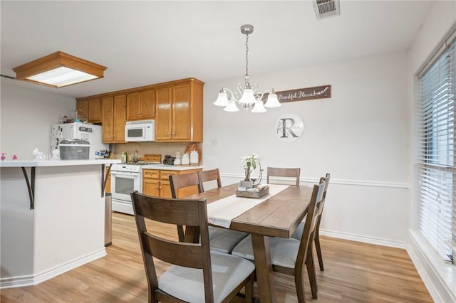 dining area featuring light wood-type flooring, a chandelier, and baseboards
