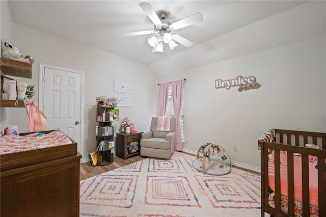 bedroom featuring vaulted ceiling, a nursery area, light wood-type flooring, baseboards, and a ceiling fan