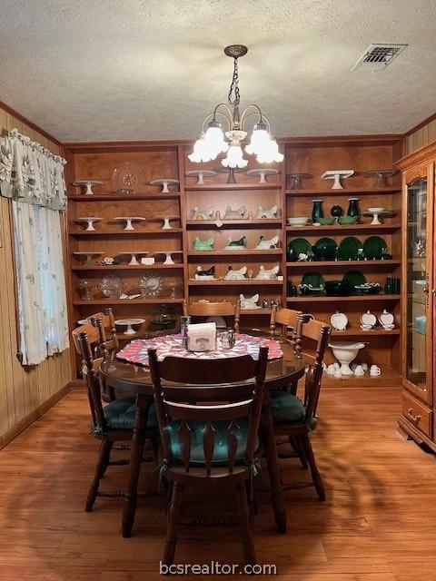 dining space featuring a notable chandelier, wood walls, wood-type flooring, and a textured ceiling