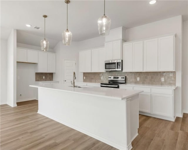 kitchen featuring appliances with stainless steel finishes, decorative light fixtures, an island with sink, and white cabinets