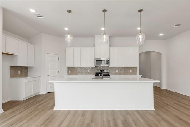 kitchen with stainless steel appliances, white cabinetry, a kitchen island with sink, and decorative light fixtures